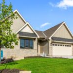 Modern beige brick home with two-car garage and manicured lawn under blue sky